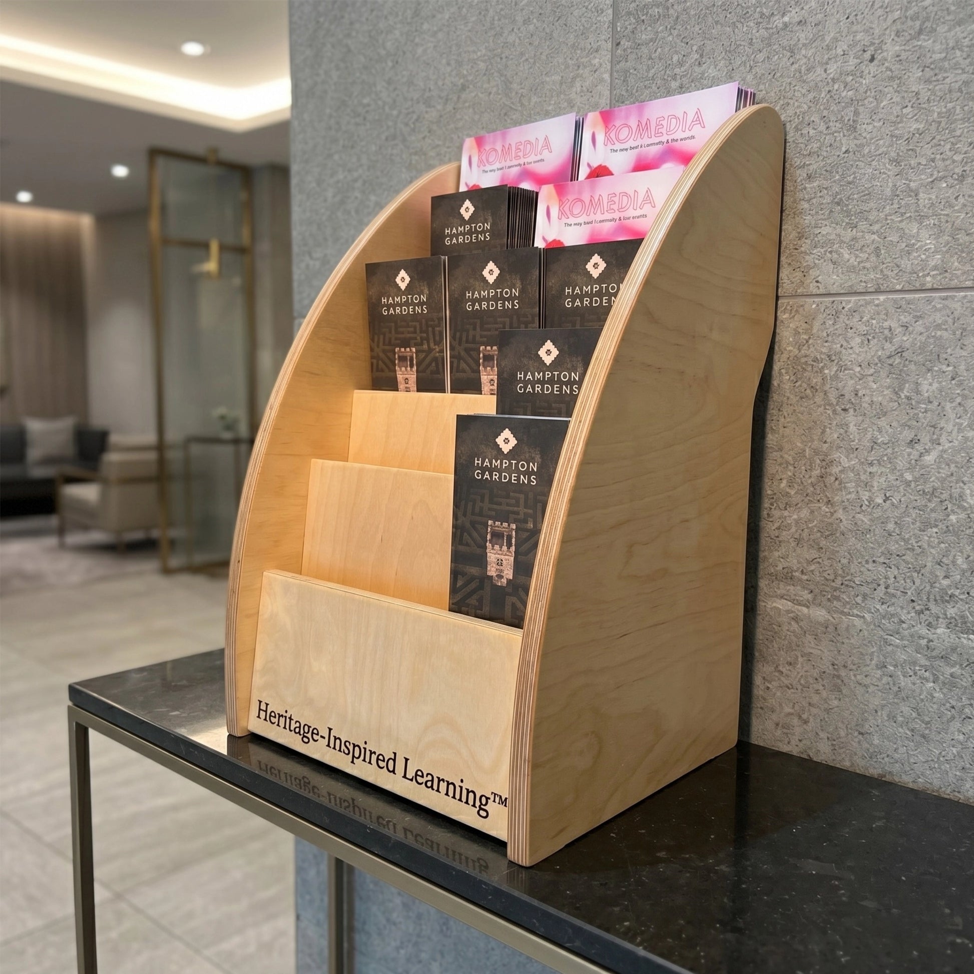 Wooden leaflet holder shown in lobby setting with custom engraving example.